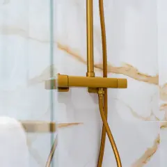 Robinet de douche doré, avec un pommeau réglable en hauteur, sur un mur carrelé de marbre blanc et or.