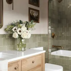 Élégante salle de bain verte avec carrelage texturé, vasque en bois, bouquet de fleurs blanches et robinetterie dorée.
