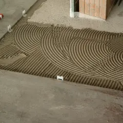 Pose de carrelage : la chape maigre attend les carreaux, avec des croisillons blancs et un lit de colle strié.