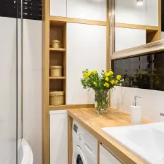 Petite salle de bain avec baignoire, lavabo, machine à laver et étagères en bois. Un bouquet de fleurs jaunes décore le plan de travail.