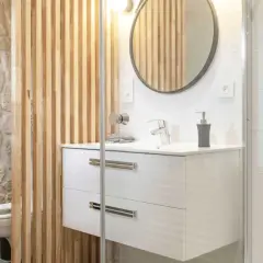 Salle de bain moderne avec un lavabo suspendu, un miroir rond et une **installation WC** discrète derrière un paravent en bois.