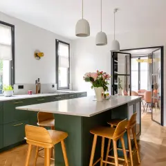 Cuisine moderne avec îlot central, tabourets en bois et armoires vert forêt. Une belle deco cuisine pour un intérieur lumineux.