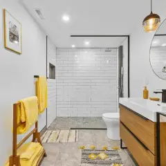 Salle de bain en longueur moderne avec douche carrelée, vasque en bois et serviettes jaunes vives.