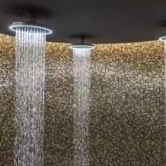 Trois douches modernes avec éclairage LED diffusent des cascades d'eau sur un mur de mosaïque. Une expérience de douche sensorielle unique.