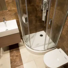 Salle de bain rouille et bois : douche d'angle, lavabo suspendu, toilettes. Ambiance chaleureuse et moderne.
