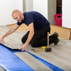 Pose d'un revêtement de sol stratifié sur une sous-couche bleue, assurant une isolation phonique sous carrelage. Outils de pose à proximité.