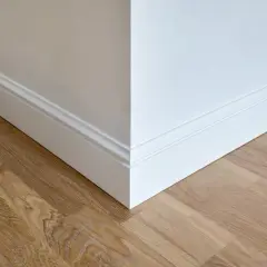 Coin de mur blanc avec plinthe moulurée et parquet en bois clair. La hauteur de la plinthe carrelage est bien visible.