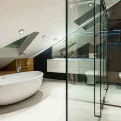 Élégante petite salle de bain mansardée avec baignoire îlot, douche vitrée, lavabo suspendu et WC.