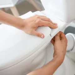 Mains ajustant le siège d'un WC. La hauteur de l'alimentation en eau du WC est correcte.