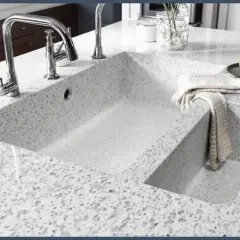 Évier double en quartz ou granit moucheté, avec robinetterie chromée et torchon plié.