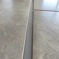 Gros plan sur un joint de dilatation carrelage gris, entre deux carreaux texturés.