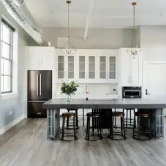 Cuisine moderne avec îlot central, tabourets et armoires blanches. Une cuisine sans hotte, avec un style épuré et industriel.