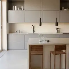 Élégante cuisine couleur taupe, avec des meubles bas et hauts épurés, un îlot central et des tabourets en bois.
