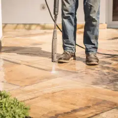 Un homme nettoie un carrelage antidérapant avec un nettoyeur haute pression. L'eau éclabousse sur les dalles.