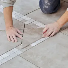 Pose en quinconce de carreaux de sol, avec une bordure décorative. Un carreleur marque une pièce avec un crayon.