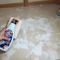 Main tenant nettoie carrelage neuf qui laisse un voile blanc avec un produit et une éponge.