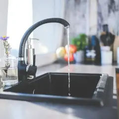 Un robinet noir verse de l'eau dans un évier, suggérant la filtration eau du robinet pour une boisson pure et saine.