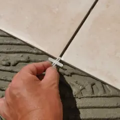 Pose de carrelage en cours, une main place un croisillon. Le prix pose carrelage m2 dépend de la complexité.