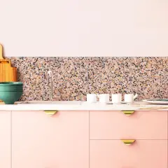 Cuisine moderne avec des armoires roses, un plan de travail en marbre et un crédence en terrazzo coloré. Ustensiles de cuisine et vaisselle disposés.
