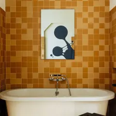 Salle de bain aux tendances carrelage ocre, baignoire blanche et miroir abstrait.