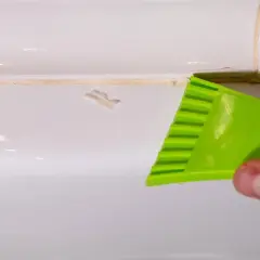 Main verte utilisée pour enlever joint silicone sale sur une surface blanche.