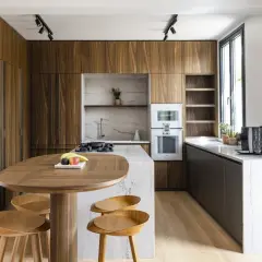 Cuisine moderne aux finitions boisées, conçue par un architecte d'intérieur. Table ovale en bois, tabourets, îlot central en marbre, et électroménagers intégrés.