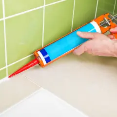 Application d'un nouveau joint blanc avec un pistolet à silicone pour refaire le joint de douche.