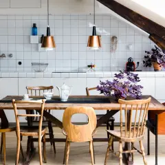 Une cuisine ouverte en L avec un îlot central en bois, des chaises vintage et des suspensions cuivrées. Une plante violette apporte une touche de couleur.