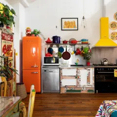 Cuisine colorée avec frigo orange vif, vaisselle suspendue et une astuce rangement cuisine : des portes de placard dépareillées pleines de charme.
