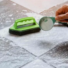 Une main verse une poudre nettoyante sur un carrelage très encrassé, prêt à être brossé.