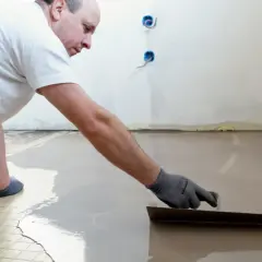Un ouvrier applique du ragréage autonivelant sur un sol, créant une surface lisse et uniforme.
