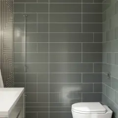Salle de bain moderne avec lavabo, miroir éclairé et WC. Le carrelage sur placo gris et vert crée une ambiance épurée.