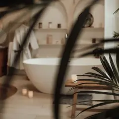 Une baignoire îlot blanche dans une **chaleureux salle de bain zen**. Un peignoir blanc est suspendu, des bougies allumées et des plantes apportent une touche de sérénité.