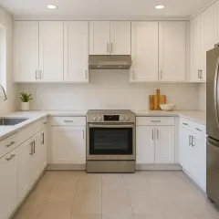Cuisine moderne avec armoires blanches, évier, cuisinière et réfrigérateur en acier inoxydable, sur un sol en carrelage blanc.