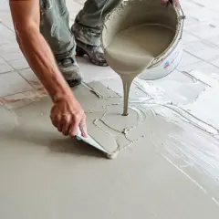 Application de béton ciré sur carrelage sol. Un ouvrier étale le produit avec une spatule, créant une surface lisse et moderne.