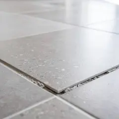 Carrelage gris, certaines dalles se soulèvent, révélant le gravier en dessous. Un signe de vieillissement, peut-être une décennale carrelage à prévoir.