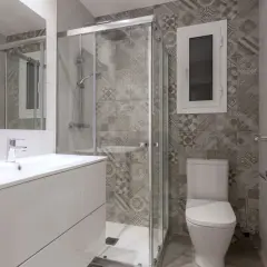 Salle de bain petite aux tons gris. Carrelage mural à motifs géométriques, douche vitrée, lavabo blanc et WC.