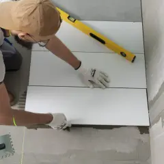 Pose d'un carrelage mural de salle de bain. Un carreleur utilise un niveau et un laser pour un calcul précis.