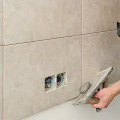 Un carreleur applique un joint époxy sur des carreaux muraux. Il utilise une taloche pour étaler le mortier.