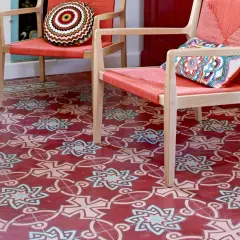Sol rouge orné de motifs géométriques complexes, typiques des pose carreaux de ciment. Deux fauteuils orange vif avec coussins colorés.