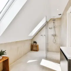 Salle de bain sous pente avec douche à faible hauteur, lavabo moderne et puits de lumière.