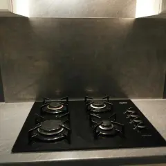 Plaque de cuisson noire avec quatre feux, devant un mur de crédence gris métallisé.