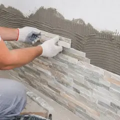Pose de pierre de parement sur un mur avec du mortier. Un artisan pose méticuleusement les pierres pour un revêtement mural naturel.