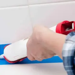 Application d'un joint silicone blanc avec un pistolet pour assurer l'étanchéité de la douche. Le bon quel joint pour douche est essentiel.
