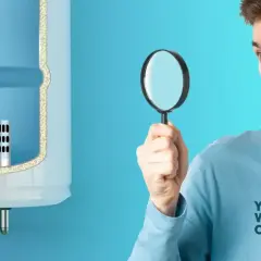 Un homme regarde avec une loupe un chauffe-eau, peut-être pour optimiser la consommation cumulus 300l.