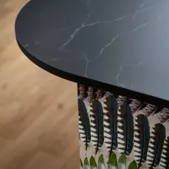 Plan de travail de cuisine en marbre noir avec un motif de plumes colorées sur le côté, créant une profondeur visuelle.
