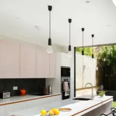 Cinq suspensions noires au design épuré, quel luminaire pour cuisine moderne ! Elles éclairent une cuisine lumineuse avec ses meubles roses et sa grande baie vitrée.