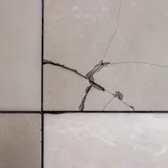 Gros plan sur un carrelage beige fissuré, montrant les étapes pour comment reparer un eclat de carrelage.