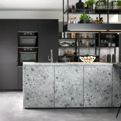 Cuisine moderne aux façades grises et à l'îlot central en sol terrazzo. Électroménagers intégrés et étagères noires remplies d'objets décoratifs.