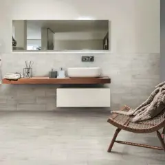 Salle de bain moderne avec murs et sol en grès cérame émaillé effet bois, lavabo suspendu, fauteuil confortable.